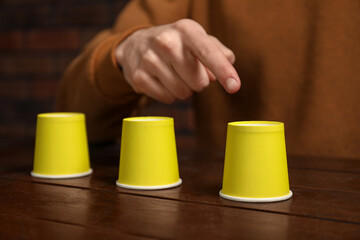 Man playing shell game at wooden table, closeup