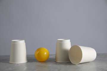 Shell game. Three paper cups and ball on grey marble table