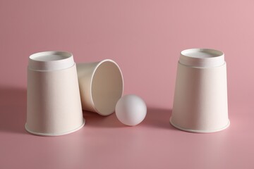 Shell game. Three paper cups and ball on pink background
