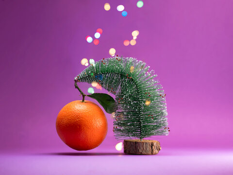 Orange hanging on a miniature Christmas tree ornament  against a purple background