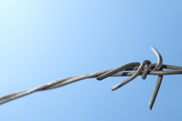 Metal barbed wire on light blue background, closeup