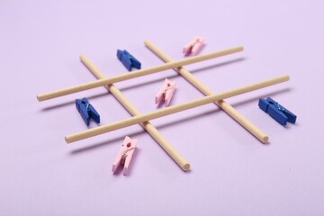 Tic tac toe game made with clothespins on lilac background