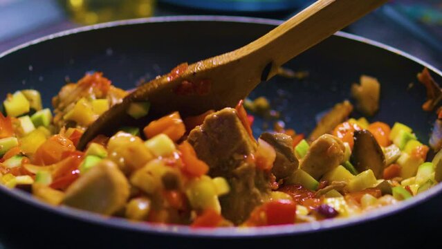 Stirring colorful vegetable stew with meat in a frying pan. Close up.