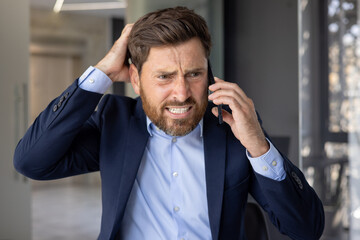 Close-up photo of a young businessman man in a suit standing in an office center, worriedly talking...