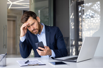 Shocked young man businessman, lawyer, banker sitting in office at desk, holding hand to head and...