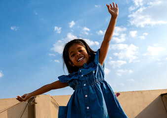 Cheerful little girl with arms outstretched in front of blue sky
