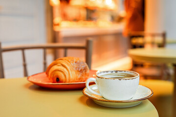 A cup of black coffee and pain au chocolat on the edge of the table in a cafe, copy space