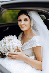 Wedding portrait. A brunette bride in an elegant dress and veil poses with a bouquet in the car....