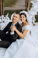 Naklejka premium lovely and stylish newlyweds are hugging and smiling against the background of autumn nature in a beautiful garden. An incredibly beautiful young bride leaned against the shoulder of her beloved groom
