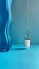 White crystal pendant, pendulum on a chain, healing amulet, spiritual energy detector on wavy blue...