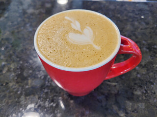 An expertly crafted cappuccino with latte art in a bright red mug on a marble countertop
