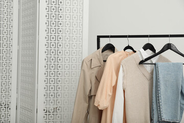 Rack with different stylish women's clothes and folding screen near light wall