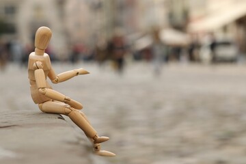 Wooden human figure sitting on curb outdoors, space for text