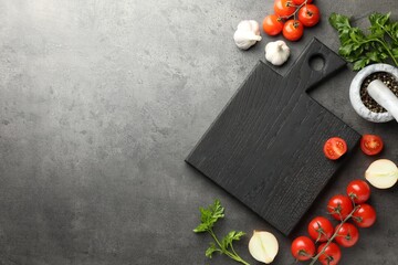 Flat lay composition with black wooden cutting board and products on dark textured table. Space for...