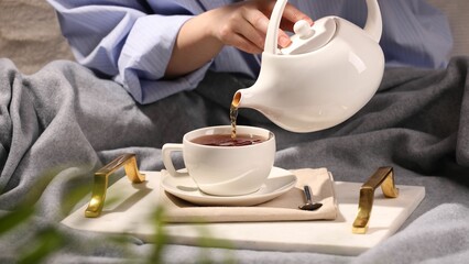 Woman pouring aromatic tea into cup at table, closeup