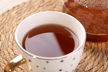 Aromatic tea in cup on wicker mat, closeup