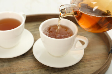 Pouring aromatic tea in cup at table, closeup