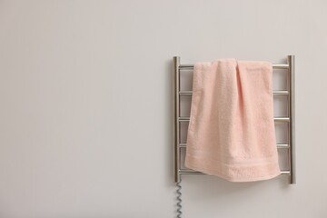 Heated rail with pink towel on white wall, space for text