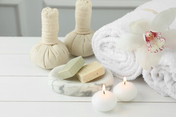 Fototapeta na wymiar Beautiful spa composition. Towels, herbal bags, soap bars and burning candles on white wooden table