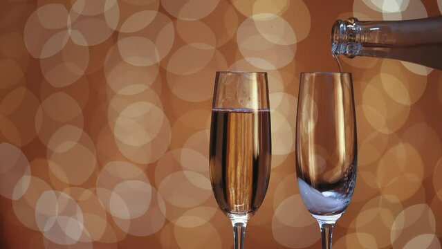 two glasses, one full of champagne and the other empty. bottle fills the glass with champagne. bokeh effect background with golden light. space to the left.