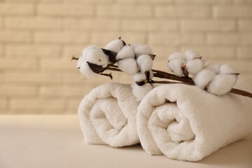 Rolled terry towels and cotton branch on white table near brick wall indoors, space for text