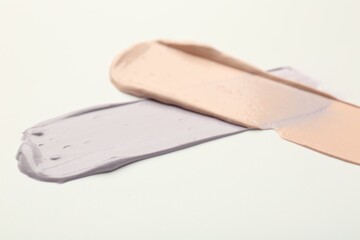 Strokes of pink and purple color correcting concealers on white background, closeup