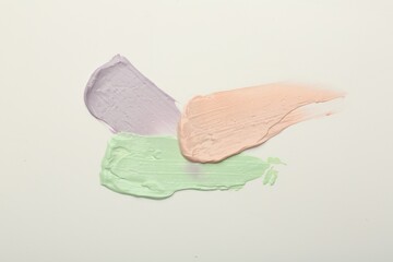 Strokes of pink, green and purple color correcting concealers on white background, top view