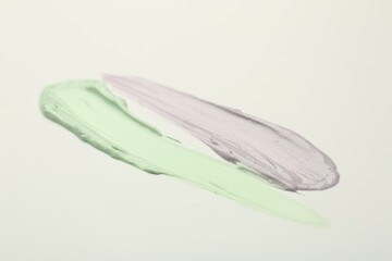 Strokes of green and purple color correcting concealers on white background