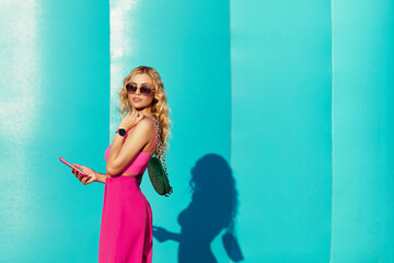 Sunny style fashion portrait of young woman on blue background. Girl wearing cute trendy pink...