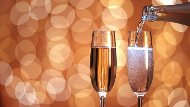 dos copas, una llena de champ&aacute;n y la otra vac&iacute;a. La botella llena la copa con champ&aacute;n. Fondo de efecto bokeh con luz dorada. espacio a la izquierda.