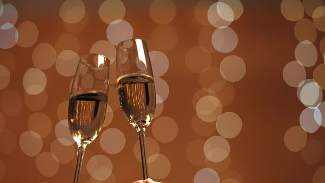 Fondo de efecto bokeh de luces doradas. Aparecen dos copas de champ&aacute;n y se brinda. espacio vac&iacute;o a la derecha de la imagen