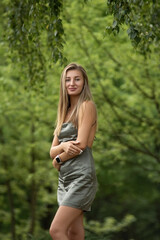 Portrait of a young beautiful blonde girl in a green dress in a city park.