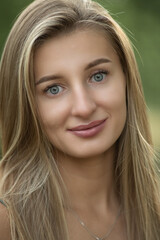 Portrait of a young beautiful blonde girl in a green dress in a city park.