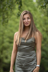 Portrait of a young beautiful blonde girl in a green dress in a city park.