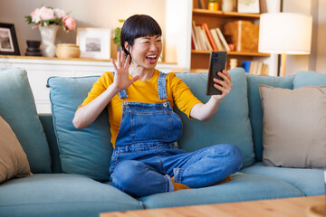 Woman having video call using smart phone while relaxing at home