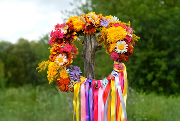 flowers wreath with colorful ribbons on wooden post on meadow. summer background. Floral crown,...