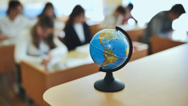 A globe of the world with textbooks in the background of a lesson in a school classroom. The globe shows North and South America.