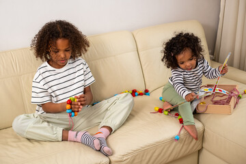 Two African American children are playing with educational toys on a cream-colored sofa. The serene...