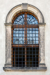 Fototapeta na wymiar Arched window with a forged metal grill against a wall of beige stone blocks. From the series window of the World.