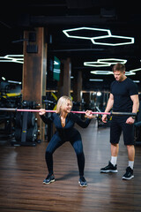 Beautiful girl is engaged in gym with personal trainer. The girl is doing exercises with the help of barbell.