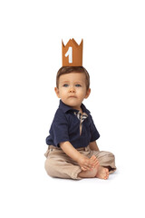 Bebé de un año sentado delante de un fondo blanco, celebrando su primer año con una corona y globos