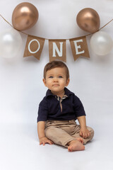 Bebé de un año sentado delante de un fondo blanco, celebrando su primer año con globos