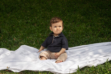 Bebé de un año sentado sobre una manta blanca en un parque en un día soleado