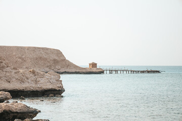 Minimalistic calm travel background with lonely small house and the ruined pier. Sandy and rocky...