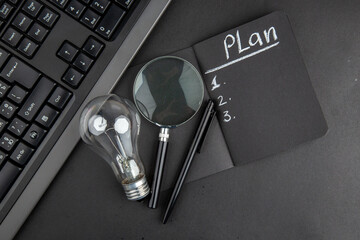 top view plan written on black notepad lupa keyboard light bulb pen on black table - obrazy, fototapety, plakaty