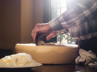 Old italian farmer cutting parmesan cheese for a meal. Traditional method of slicing wheel of...