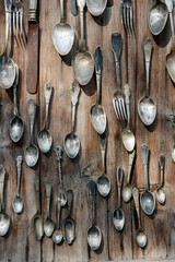 Assorted vintage silverware hanging on wooden wall. Collection of antique spoons and forks. Rustic...