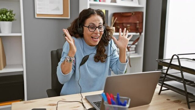 Excited woman with headphones reacting at workplace with laptop and office supplies