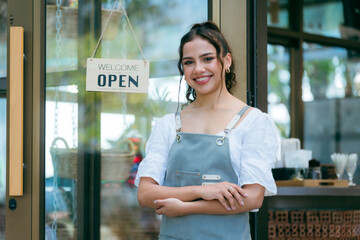 Hand of coffee shop staff woman wearing apron turning open sign board on glass door in modern cafe,...