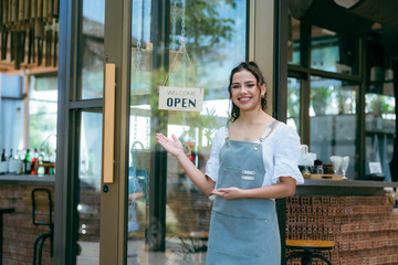 Hand of coffee shop staff woman wearing apron turning open sign board on glass door in modern cafe,...